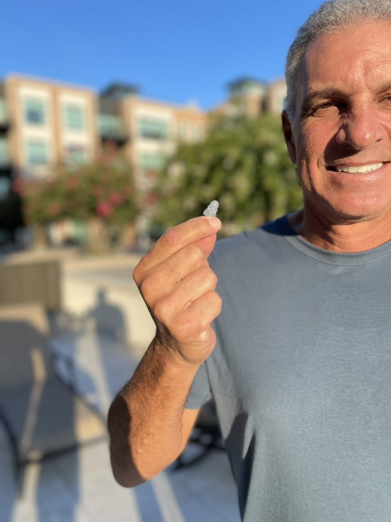 Smiling man holding a clear Auricula earplug outdoors